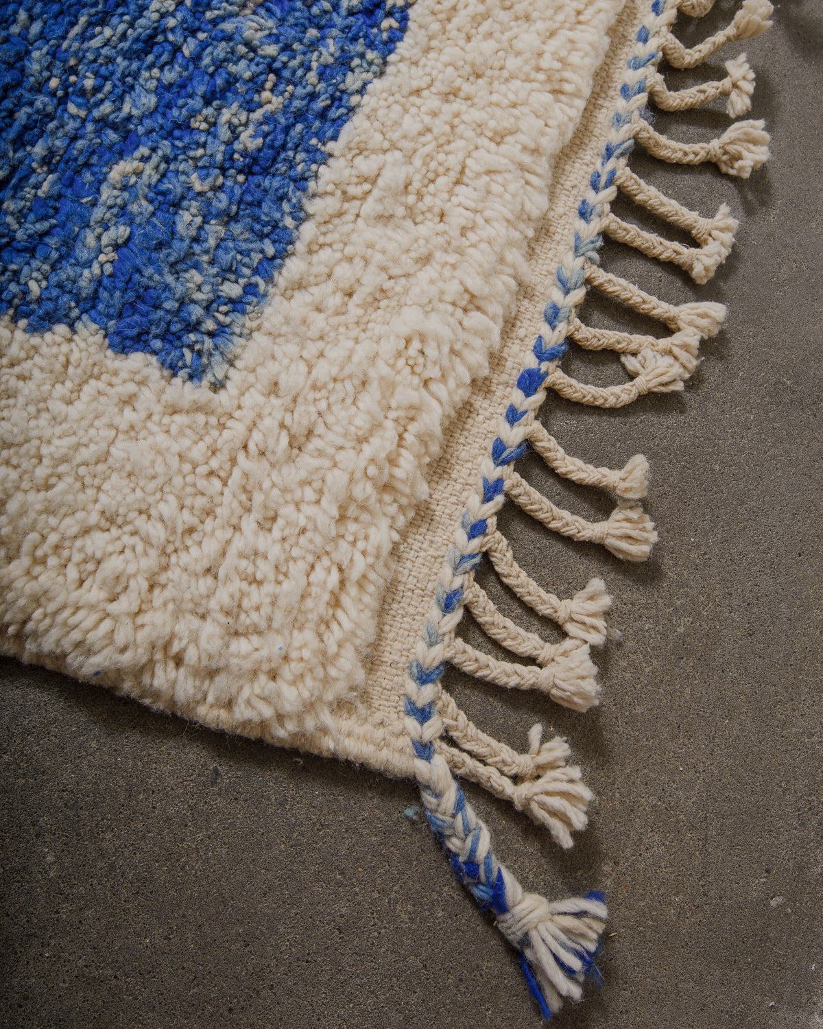 Corner of Berberlin beniourain rug with tassels on cement floor.